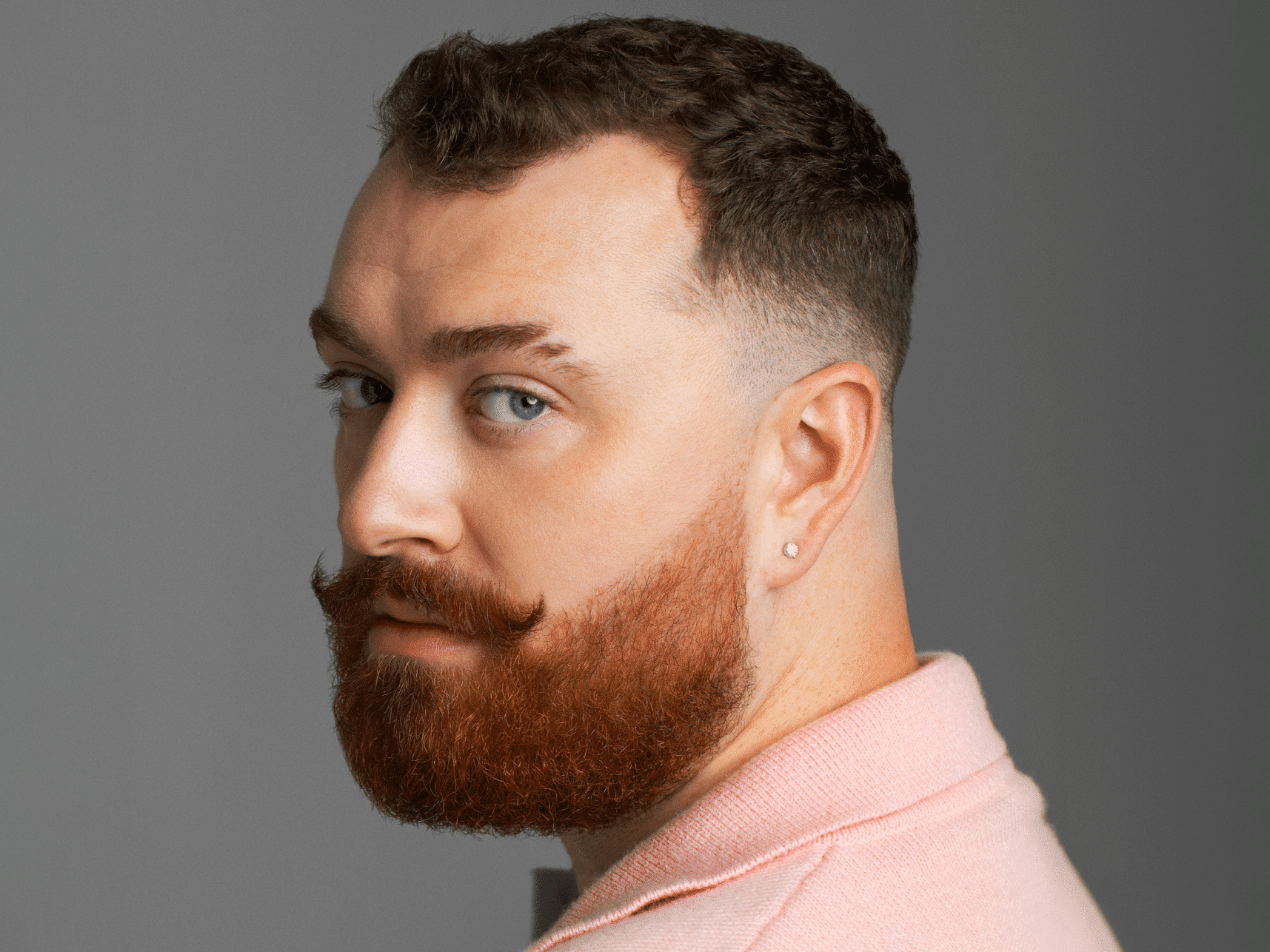 Sam Smith in pink collared shirt, looking over shoulder